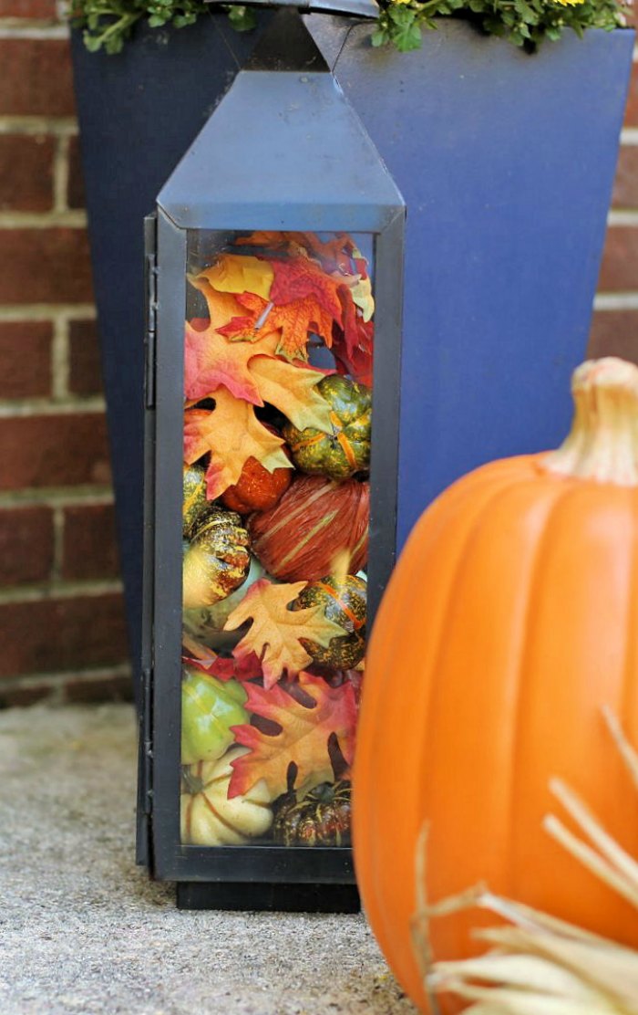 Black lantern filled with leaves, pumpkins and gourds