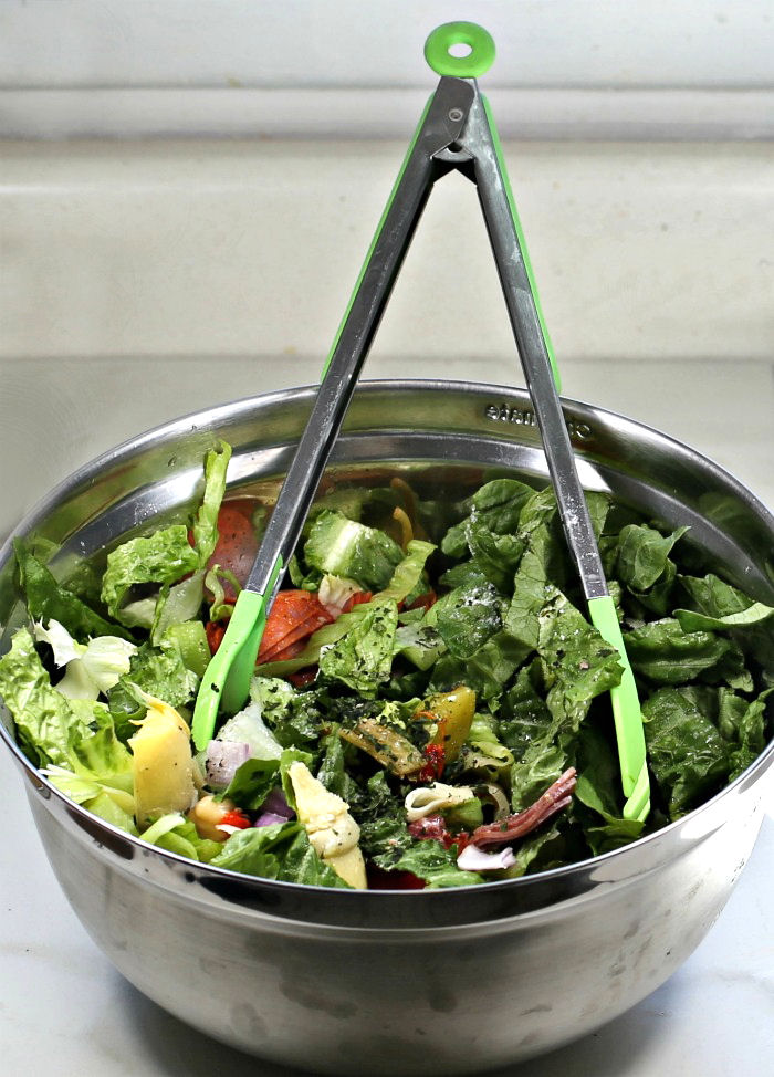 mixing a salad with cheese and cured meats