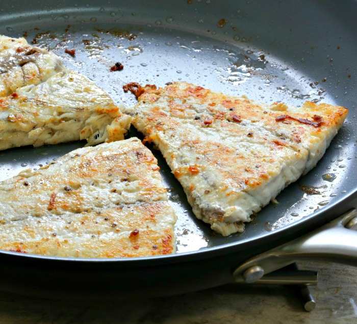 cooked barramundi fillets in a skillet.