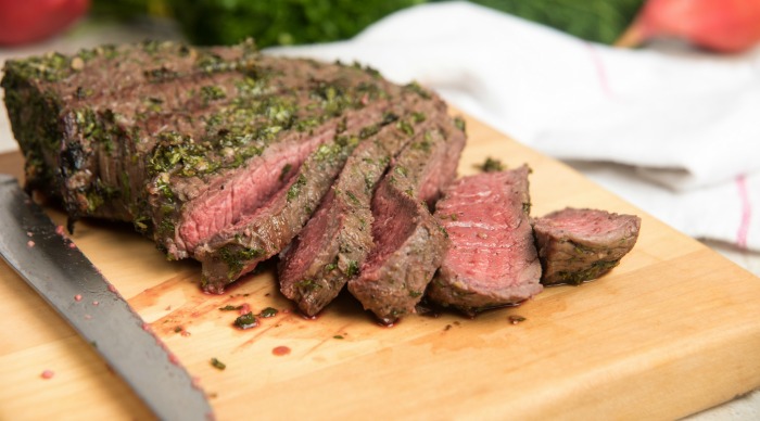 Grilled London Broil on a cutting board with a knife.