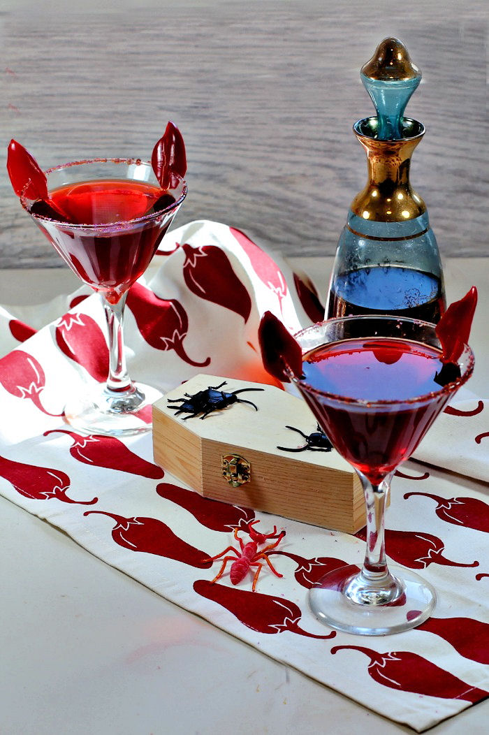 Halloween cocktail garnishes - devil horns garnish on a red drink with chili pepper towel and decanter.
