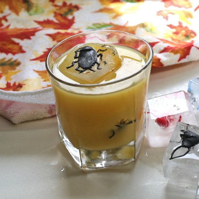 Halloween cocktail special effects - spider ice cubes in orange drink with leaf towel.