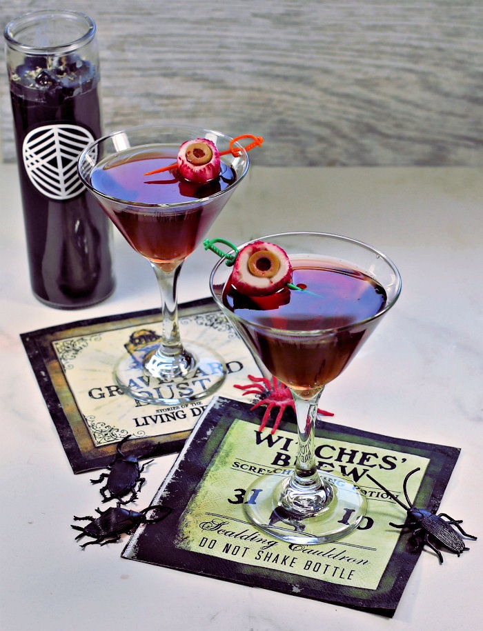 Halloween cocktail garnishes - radish eyeballs on skewers in a red drink with Halloween napkins and candle.