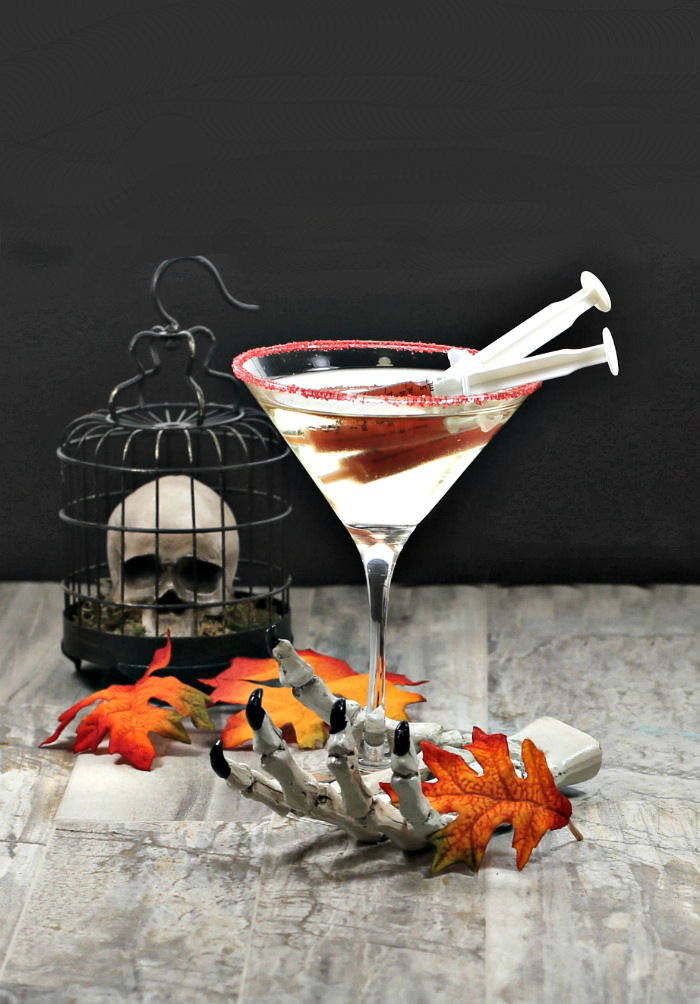 Halloween cocktail garnishes - blood filled syringes in champagne with a skeleton hand and skull.