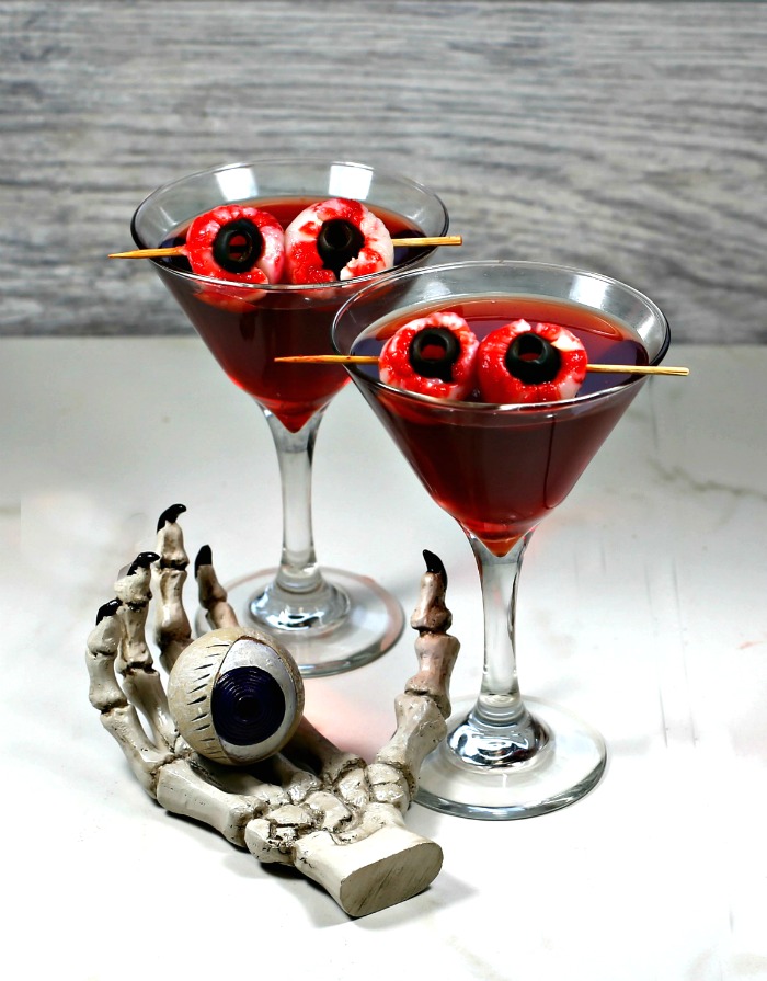 Crow's blood Halloween drink with lychee eyeball garnish and skull hand with eye.