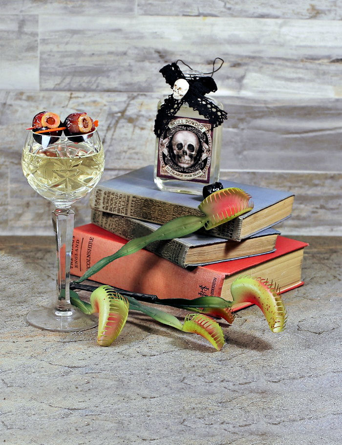 Glass of wine with grape eyeball garnish, some books bottle, and a Venus fly trap.