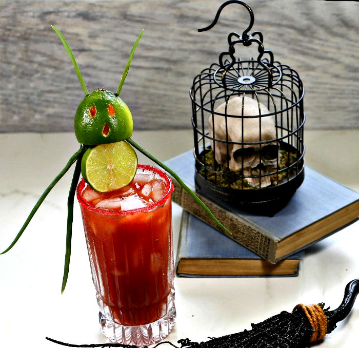 Halloween bloody Mary with a lime demon garnish and a skull bird cage on books.
