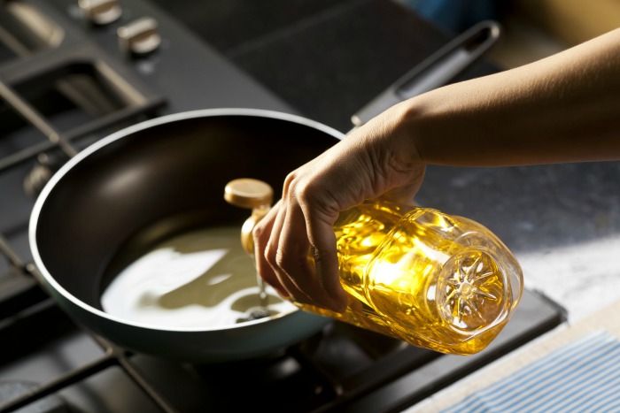 Woman pouring oil into a frying pan.