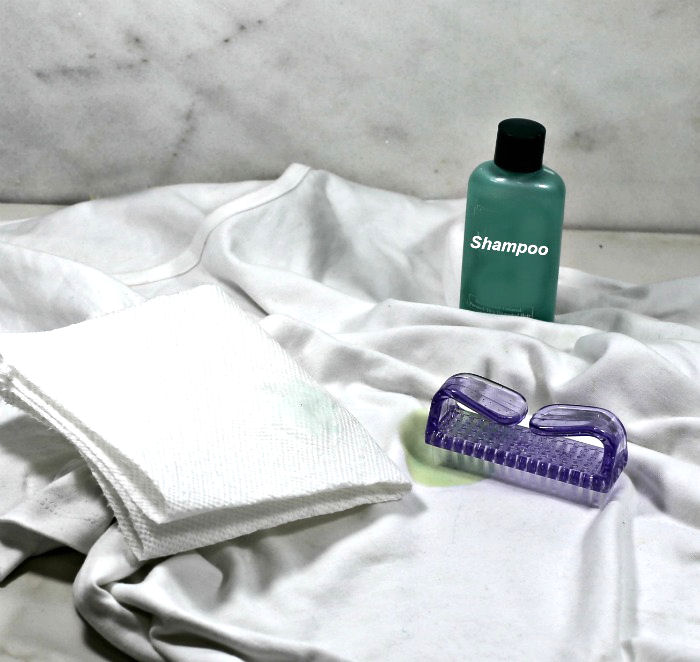 White shirt with brush, paper towel and bottle of shampoo.