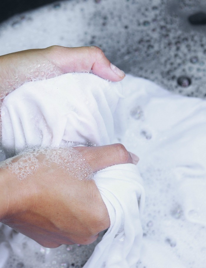 Hands in sudsy water with oil stained clothing