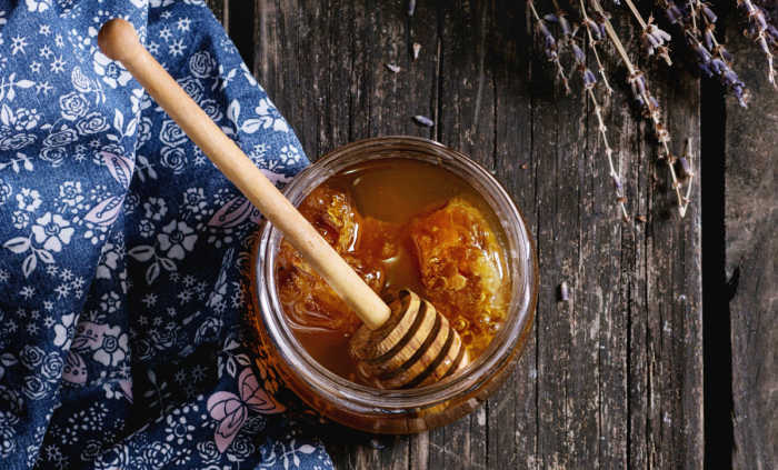 Honey with dipper on a wood board and blue cloth.