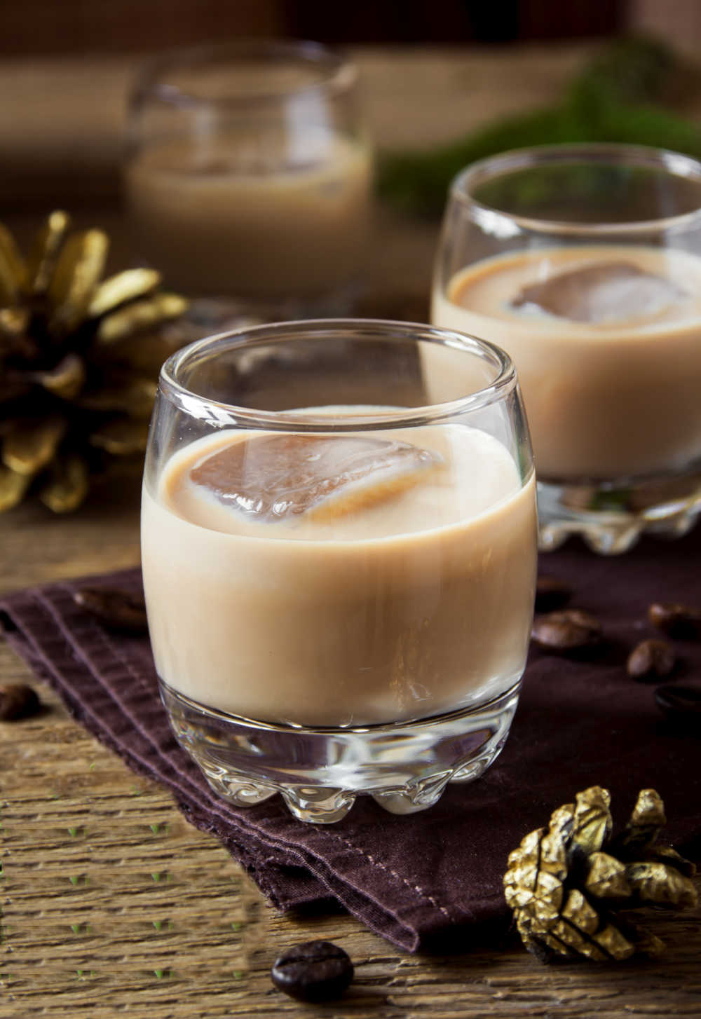 Homemade Baileys Irish cream in two glasses with ice near some pine cones.