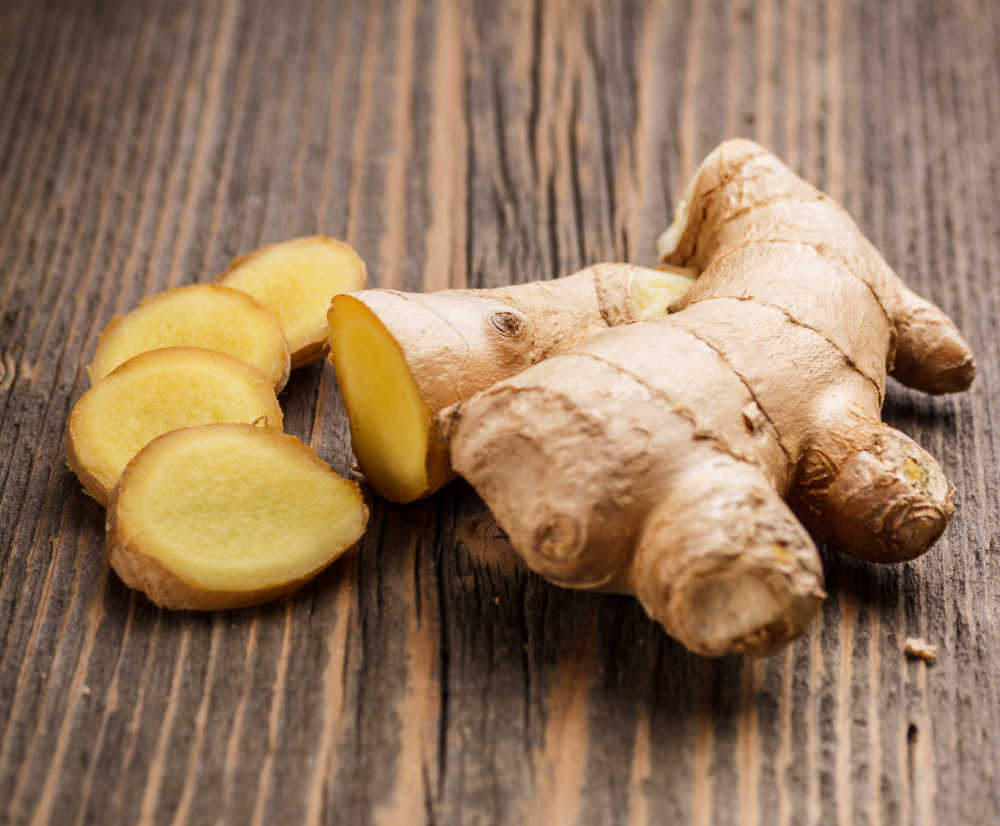 Piece of whole and sliced ginger root on a wooden board.