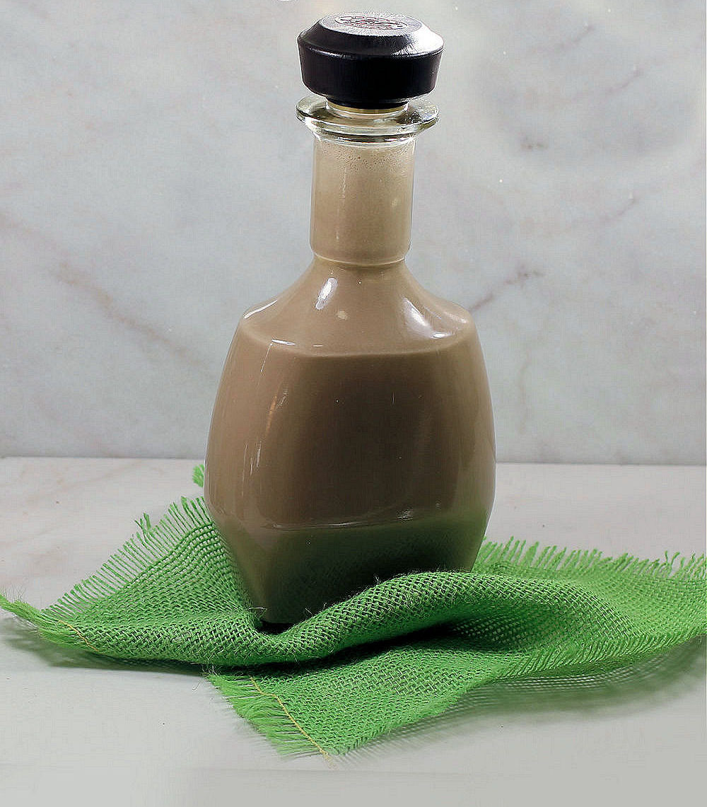 Bottle of creamy mixture on a green piece of cloth with words reading Homemade Baileys Irish Cream.