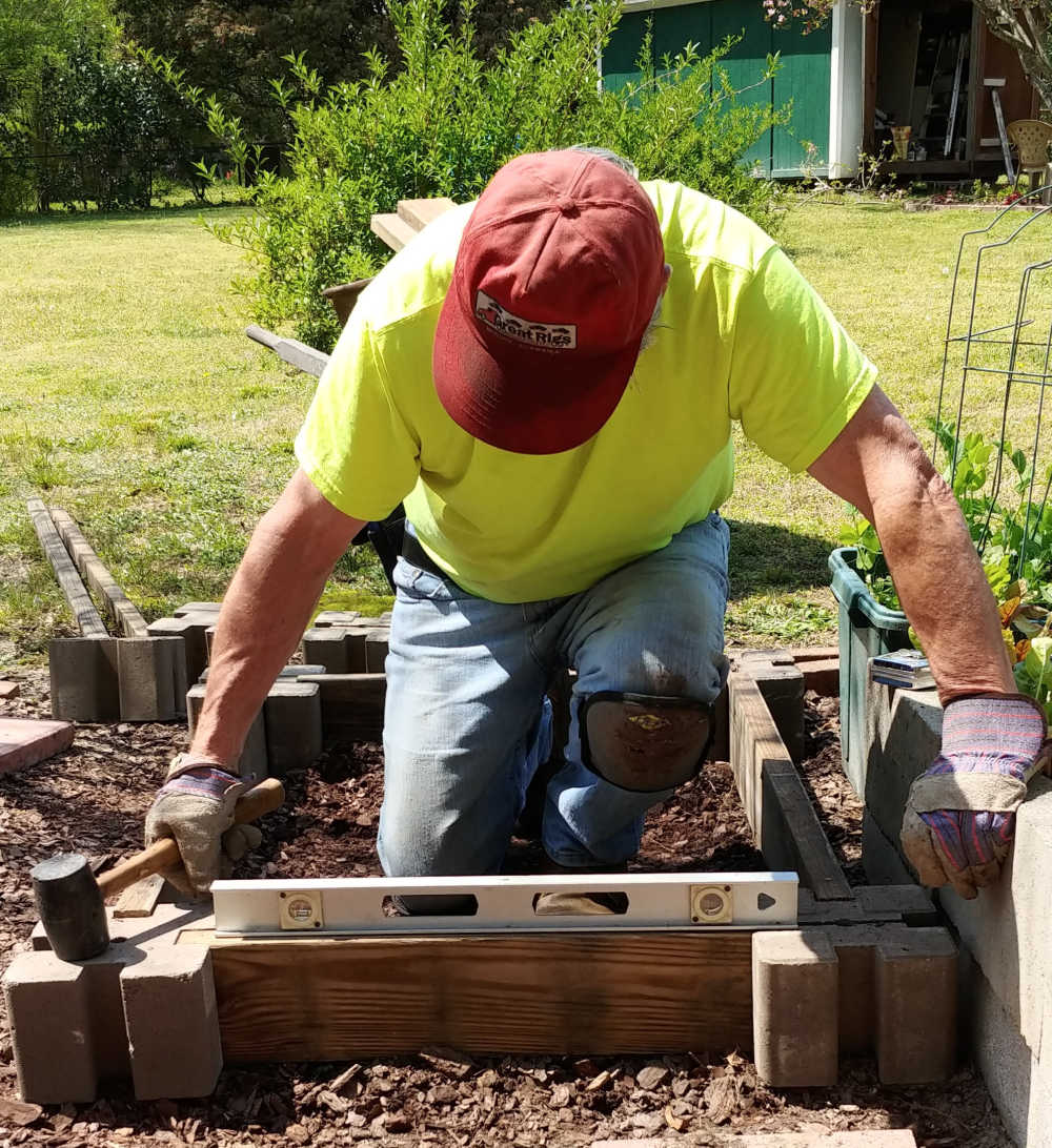 Man leveling the sides of a raised garden bed.