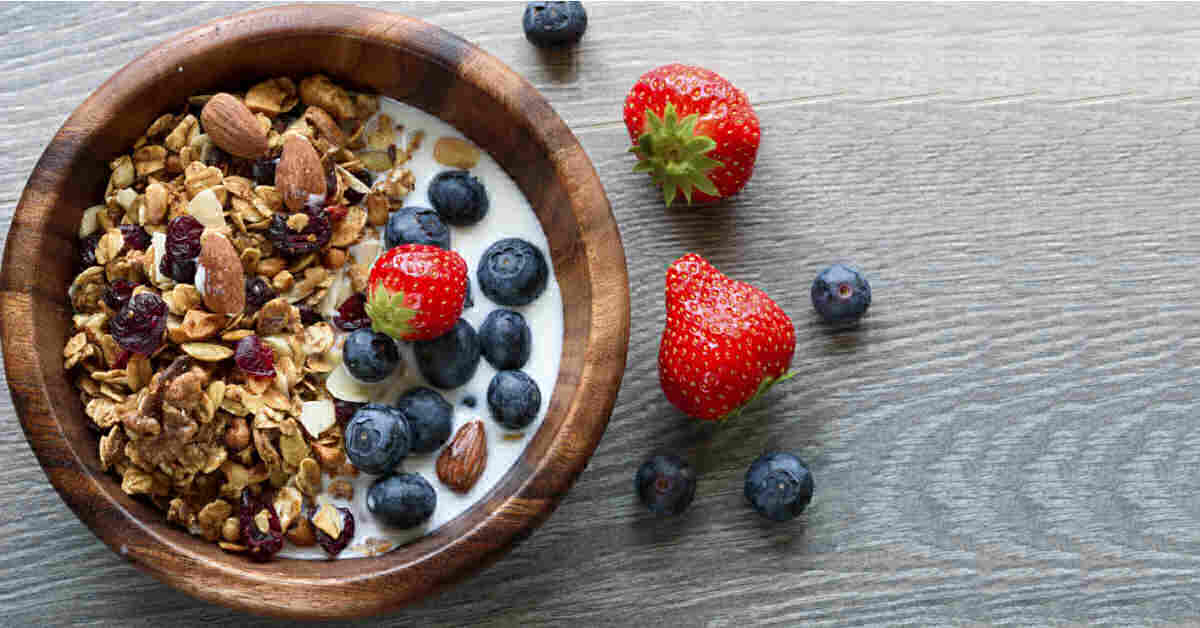 Healthy granola in a bowl with blueberres strawberries and almond milk.