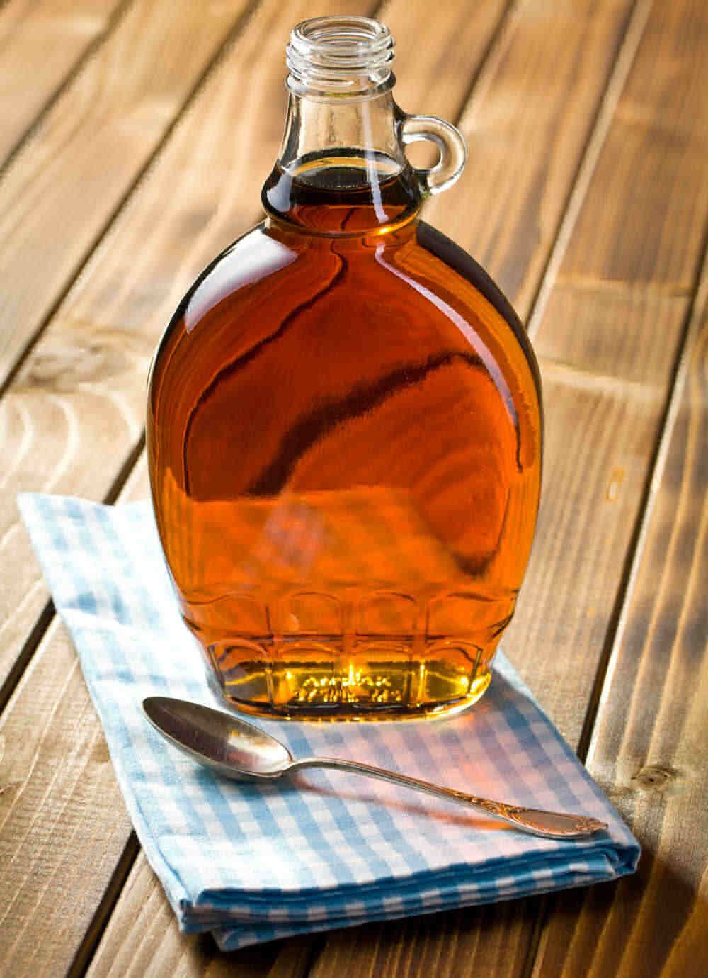 Maple syrup in a bottle on a blue napkin with a spoon.