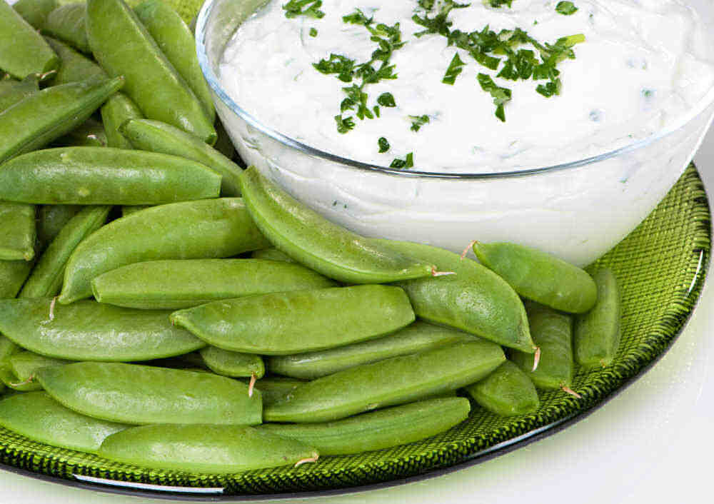 Sugar snap peas with yogurt on a clear plate.