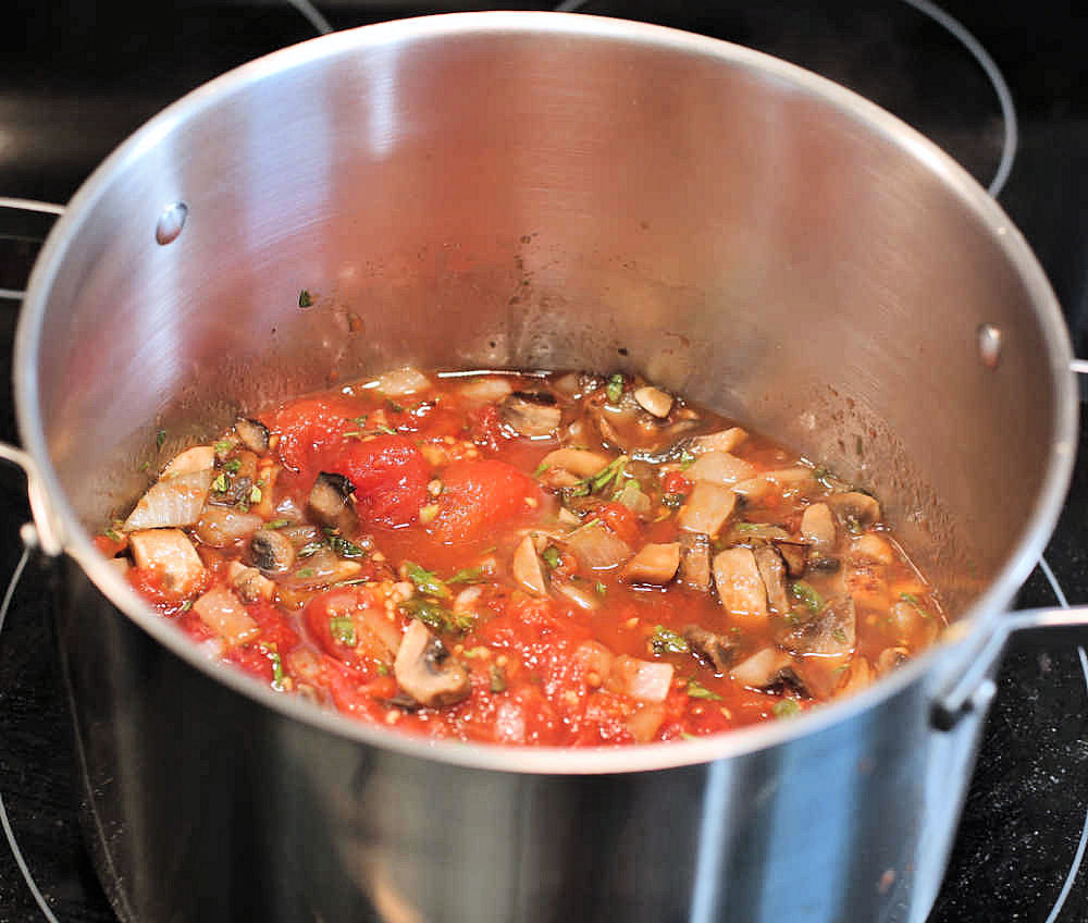Making a meaty spaghetti sauce - adding onions, herbs, mushrooms and fresh roasted tomatoes in a big pot.