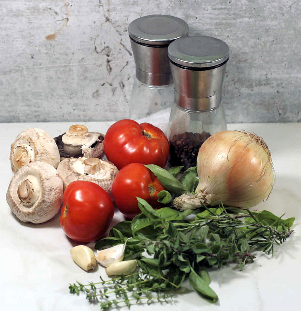 Fresh tomatoes, onions, garlic, mushrooms, salt and pepper on a counter top.