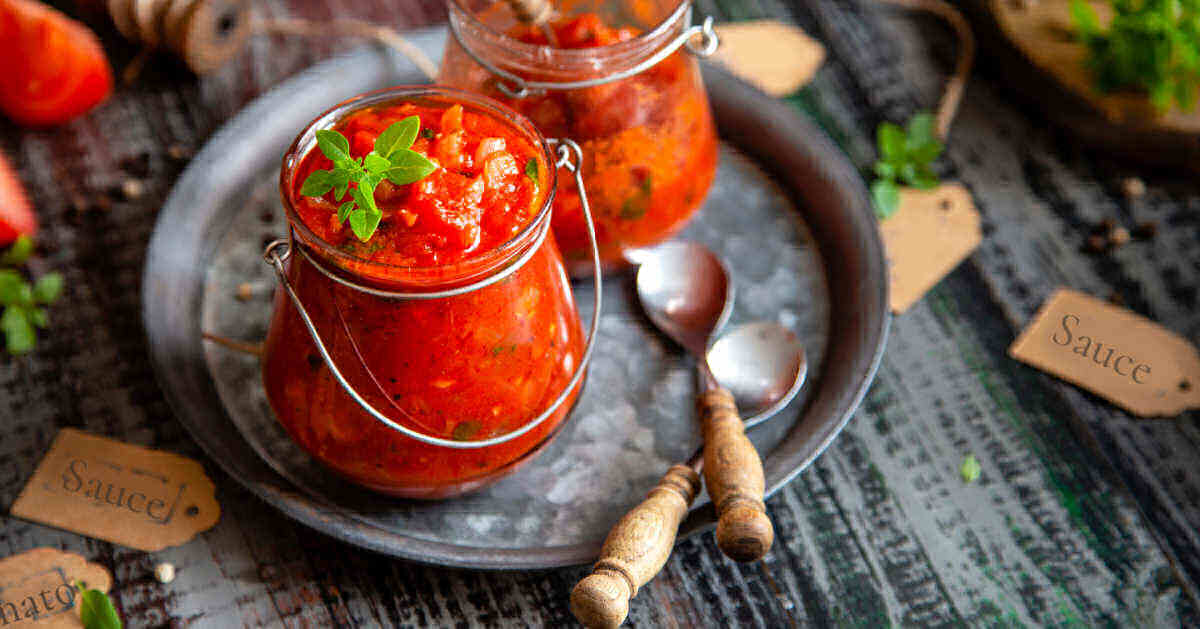 Roasted tomato pasta sauce in jars with spoons on a metal tray.