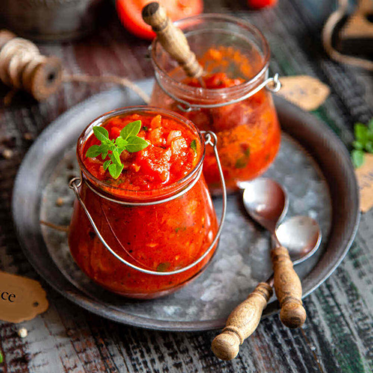 2 jars of homemade spaghetti sauce with spoons on a tray.