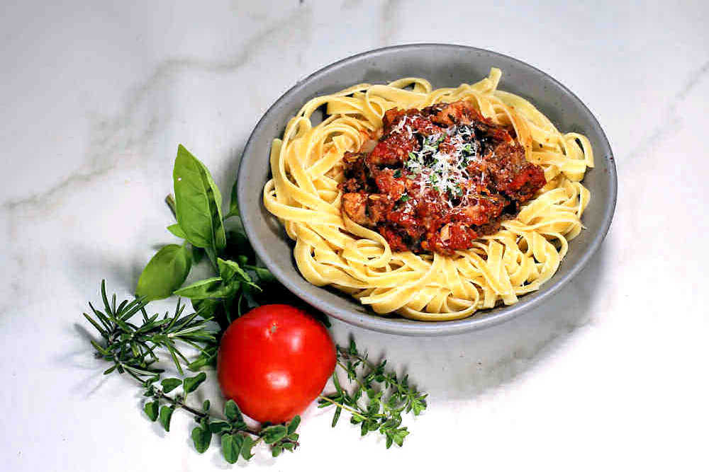Bowl of fettuccini with homemade roasted tomato pasta sauce and parmesan cheese with herbs and a fresh tomato.