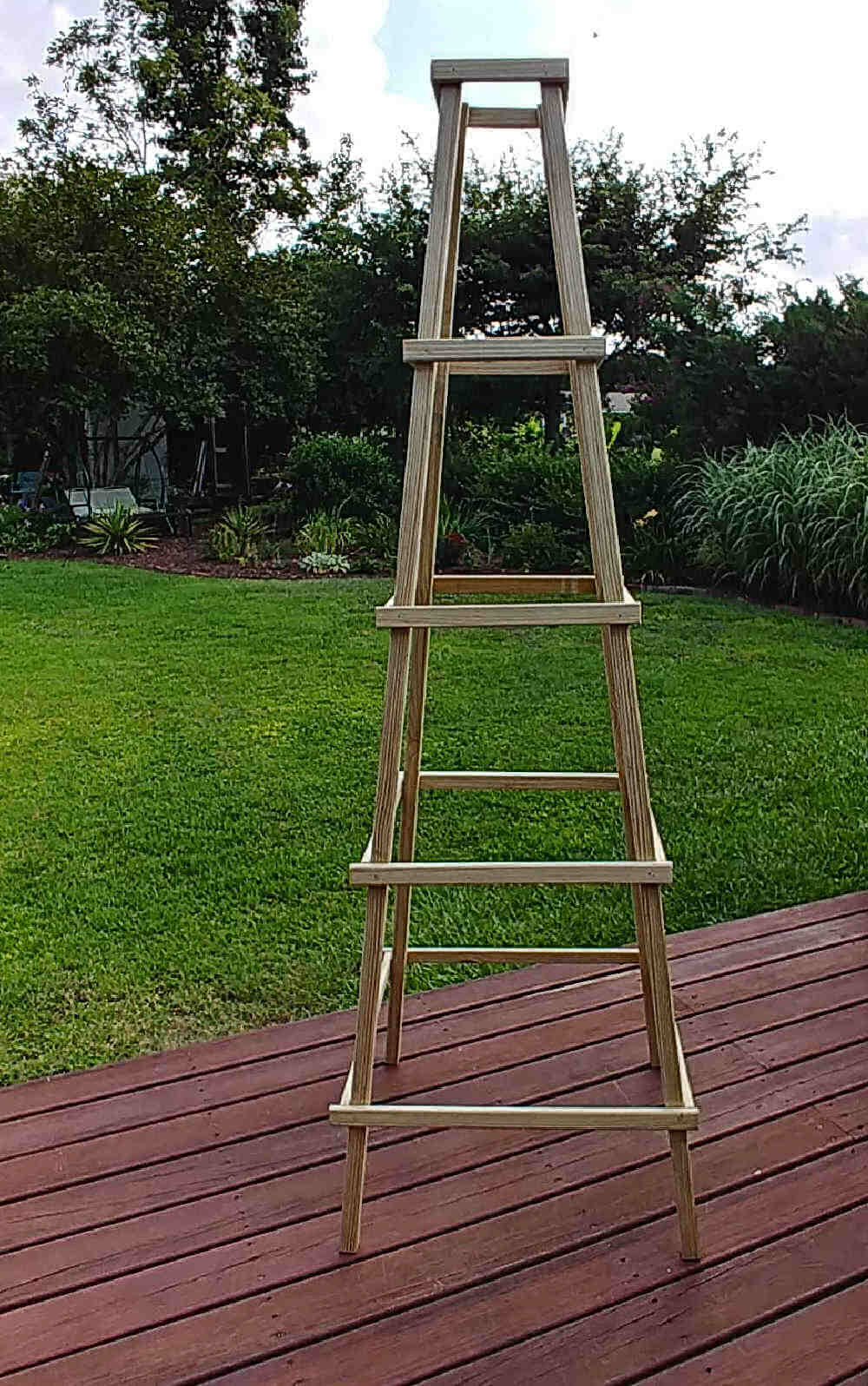 Wooden garden obelisk sitting on a wood deck.