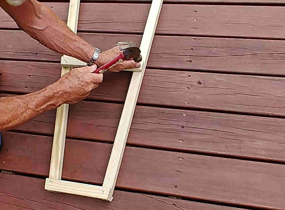 Man nailing ladder rungs for a wooden garden obelisk.