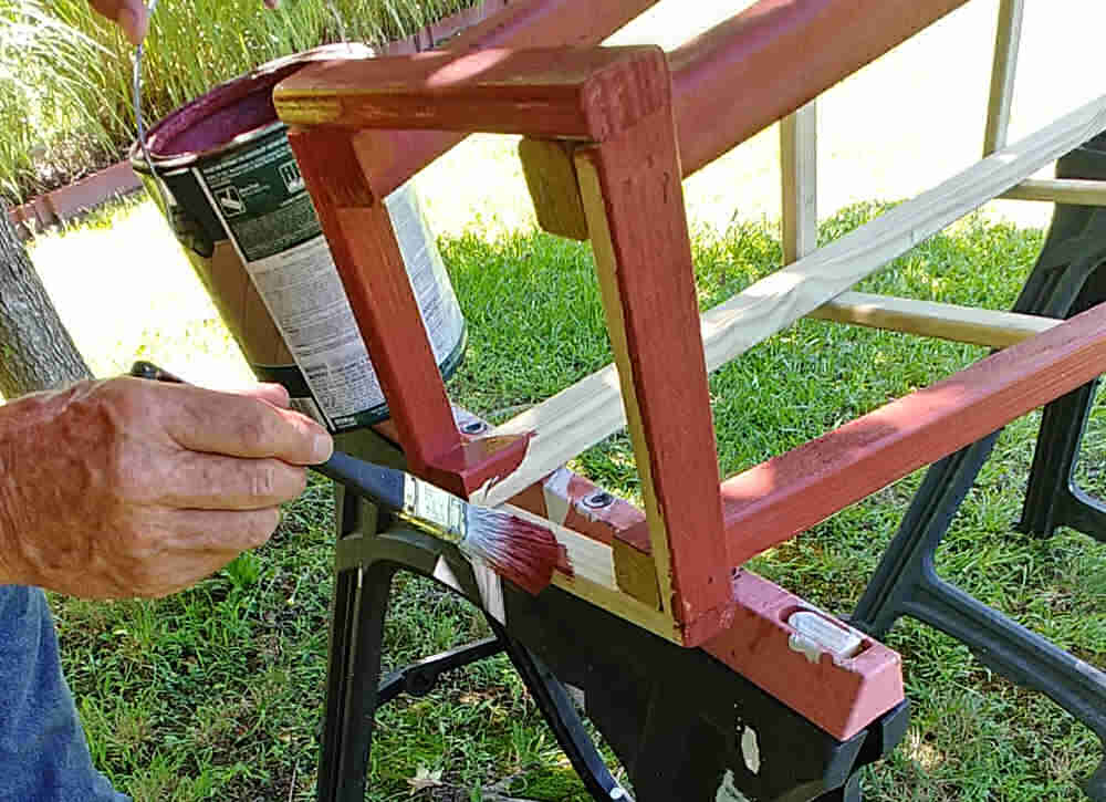 Man painting a garden tuteur with solid color wood stain.