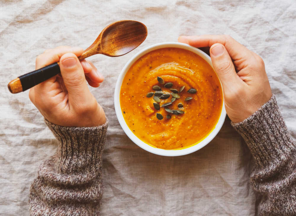 Hands with a spoon and bowl of pumpkin puree and pumpkin seeds.