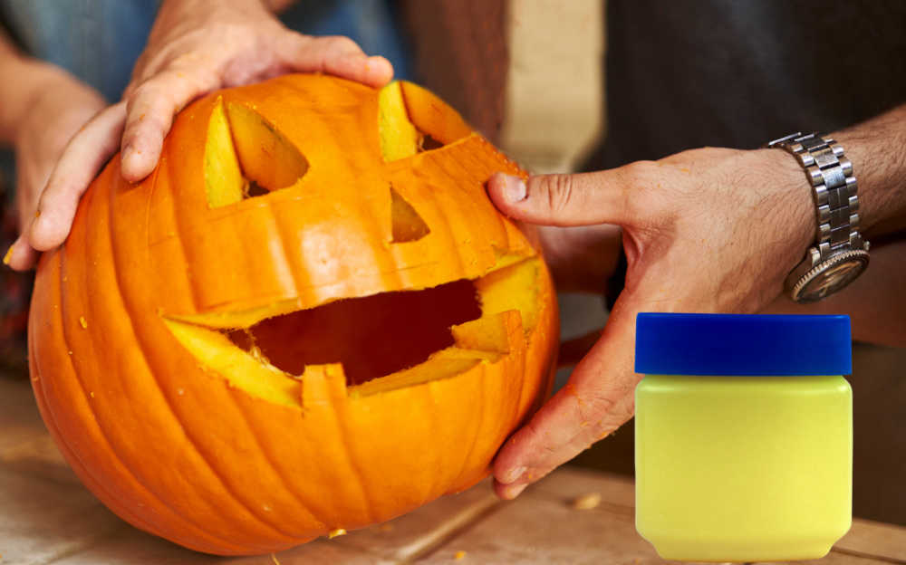 Man rubbing petroleum jelly on carved pumpkin to preserve it.