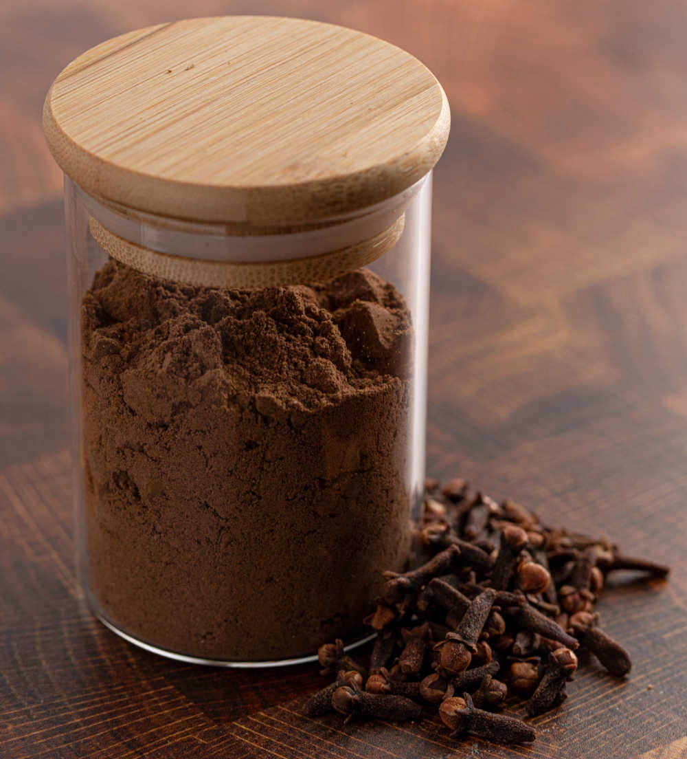 Ground and whole cloves. Ground cloves in a jar sitting next to whole cloves.
