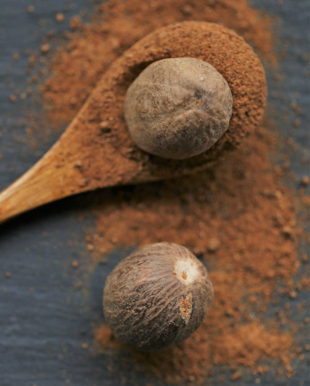 ground and whole nutmeg ground nutmeg in a wooden spoon with whole nutmeg.