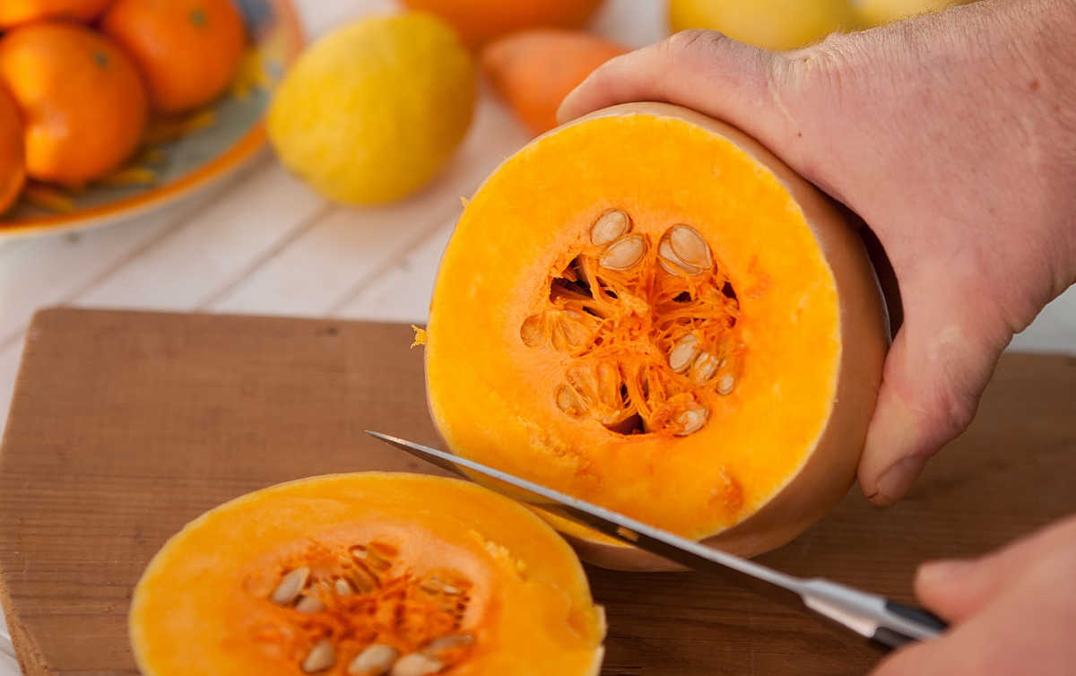 Man holding a knife and a cut pumpkin.